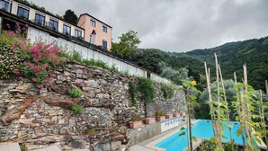 A stone retaining wall with a pool, a building with a balcony, and a mountainous backdrop. - Villino Rosanna with Private Pool and Sea View (Bogliasco)