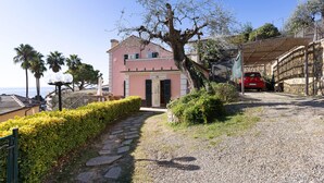 A building with a pink facade, a stone pathway, and a red car parked nearby. - Villino Rosanna with Private Pool and Sea View (Bogliasco)