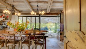 Una cocina rústica con vigas de madera, una mesa de comedor con sillas y un ventanal con vistas al follaje.