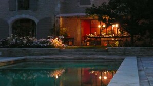 Una piscina con reflejos, un edificio con ventanales arqueados y un comedor con mesas y sillas.