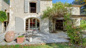 Un edificio de piedra con techo de tejas, una entrada arqueada y un patio con mesas al aire libre.