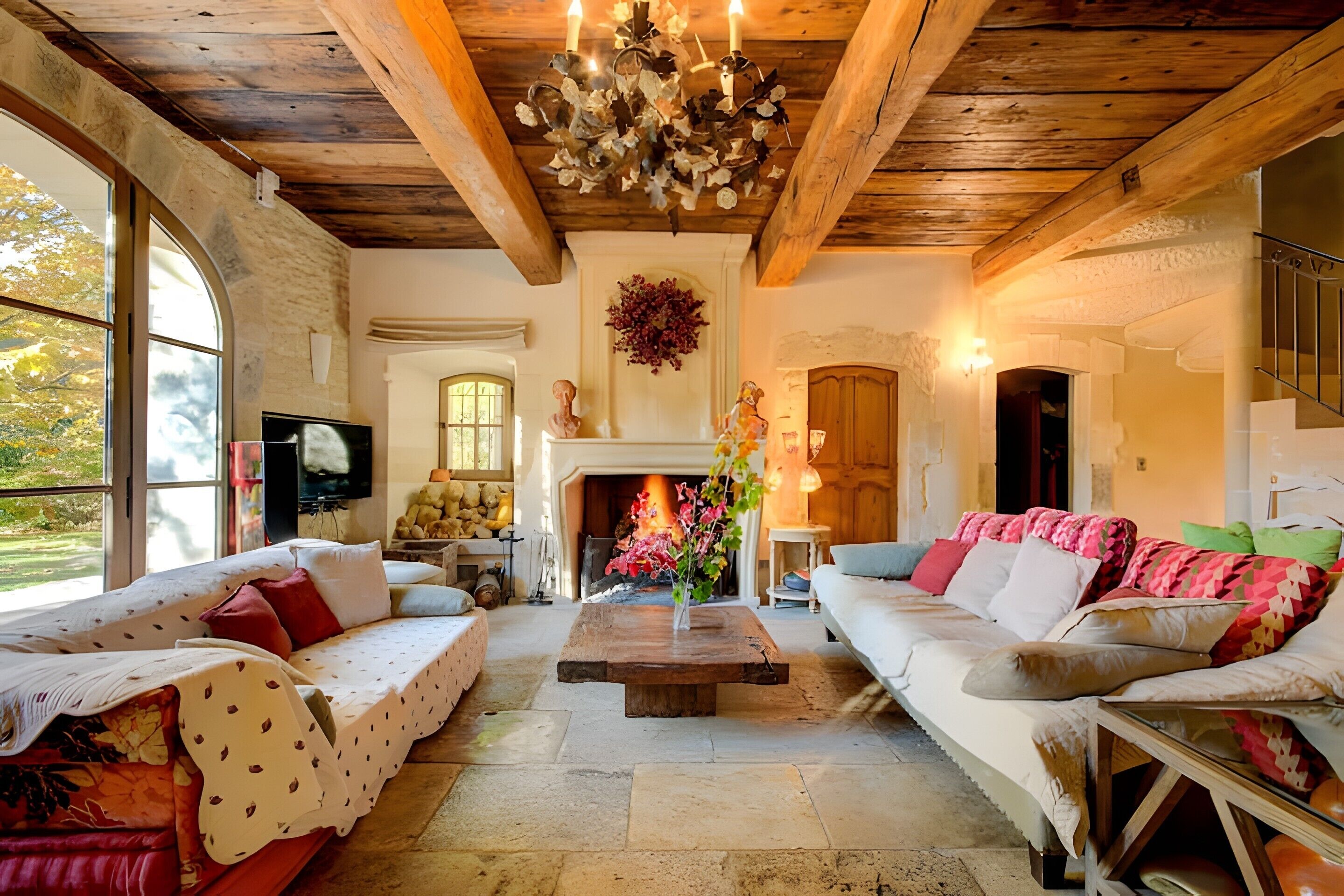 Un salon chaleureux avec une cheminée, des poutres apparentes en bois et une grande fenêtre.