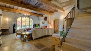 Una habitación amplia con pared de piedra, vigas de madera en el techo, una escalera y una zona de comedor con mesa y sillas.
