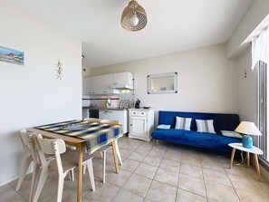 Um espaço de estar compacto com uma mesa de jantar, cadeiras, um sofá, uma cozinha pequena e uma janela.