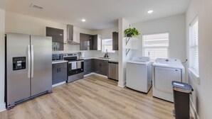 A modern kitchen with stainless steel appliances, a built-in oven, and a microwave. There are two washing machines and a trash bin. - Trendy Boho Stay - Pergola • Pool • Fire Pit (Houston)