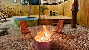 Un jardin avec un foyer, deux chaises, une piscine et une terrasse couverte.