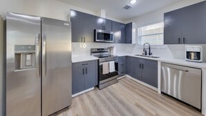 Une cuisine moderne dotée d’appareils électroménagers en acier inoxydable, de meubles gris et d’un plan de travail blanc.