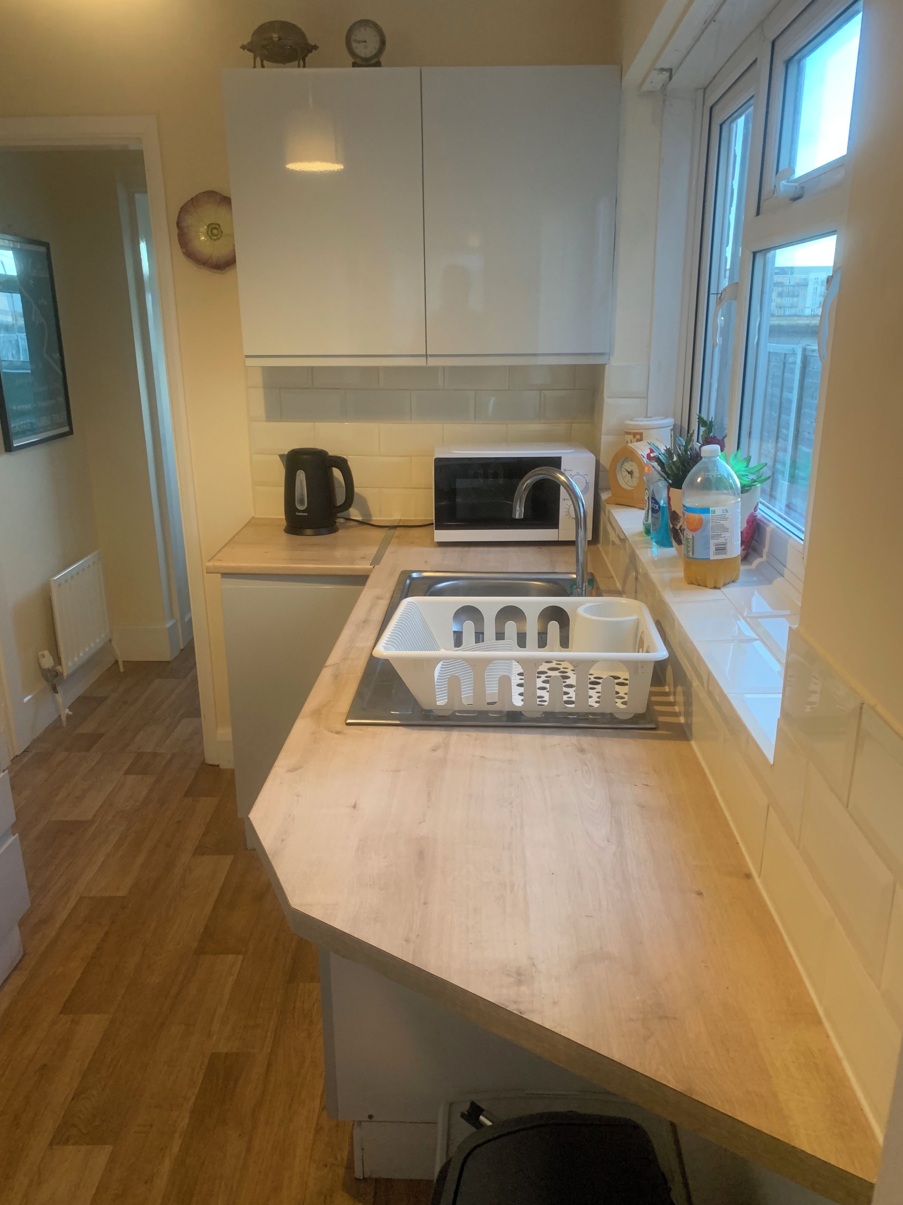 A compact kitchen with white cabinets, a microwave, a kettle, and a sink.