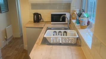 A compact kitchen with white cabinets, a microwave, a kettle, and a sink.