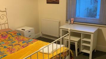 A bedroom with a bed, a desk, a radiator, and a window with blinds.