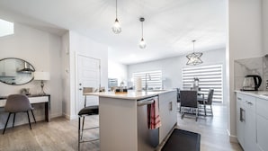 A modern kitchen with a central island, pendant lights, and a dining area with a table and chairs. - Modern Executive Home-Sleeps12-KingBeds-FullHouse (Edmonton)