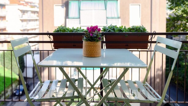 Uma varanda com mesa e cadeiras, plantas em vasos e vista para edifícios.