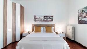 Quarto com cama, mesas de cabeceira, painel de cabeceira, radiador e um quadro na parede.