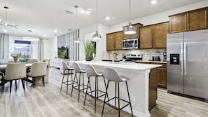 Una cocina moderna con una isla central, electrodomésticos de acero inoxidable, armarios de madera e iluminación colgante.