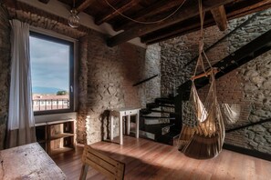 Una habitación rústica con paredes de ladrillo visto, una mesa de madera, una hamaca colgante y vistas a través de una ventana.