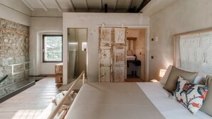 A bedroom with a bed, a wooden bench, a stone wall, a door, and a window.