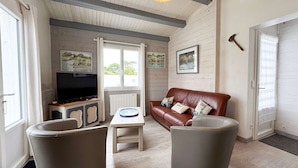 A cozy living room with a leather sofa, a television, and a small table. - Pretty single-storey villa with garden (LA COUARDE SUR MER)