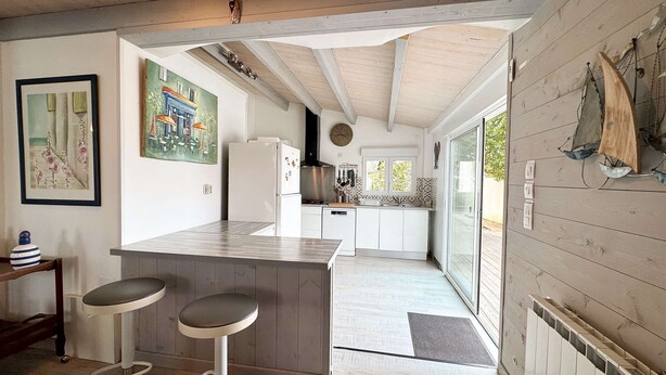 A kitchen with a wooden island, bar stools, a refrigerator, and a window overlooking a deck. - Pretty single-storey villa with garden (LA COUARDE SUR MER)