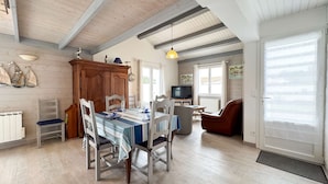 A dining area with a wooden table, chairs, and a television in the background. - Pretty single-storey villa with garden (LA COUARDE SUR MER)