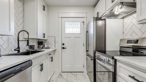 Una cocina moderna con armarios blancos, un refrigerador de acero inoxidable, horno empotrado y lavavajillas.