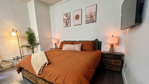 A modern bedroom with a large bed, two bedside tables with lamps, a flat-screen TV, and three wall art pieces. - Boho Haven with Free Parking, Wifi and King Bed, Walk to Clubs, U of A and Food (Tucson)