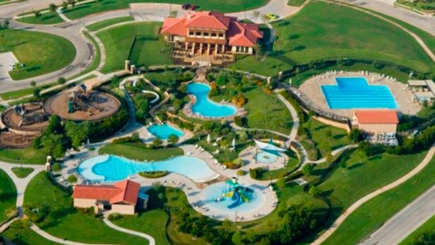 An aerial view of a resort with multiple swimming pools, a large building with a red roof, and well-maintained landscaping.