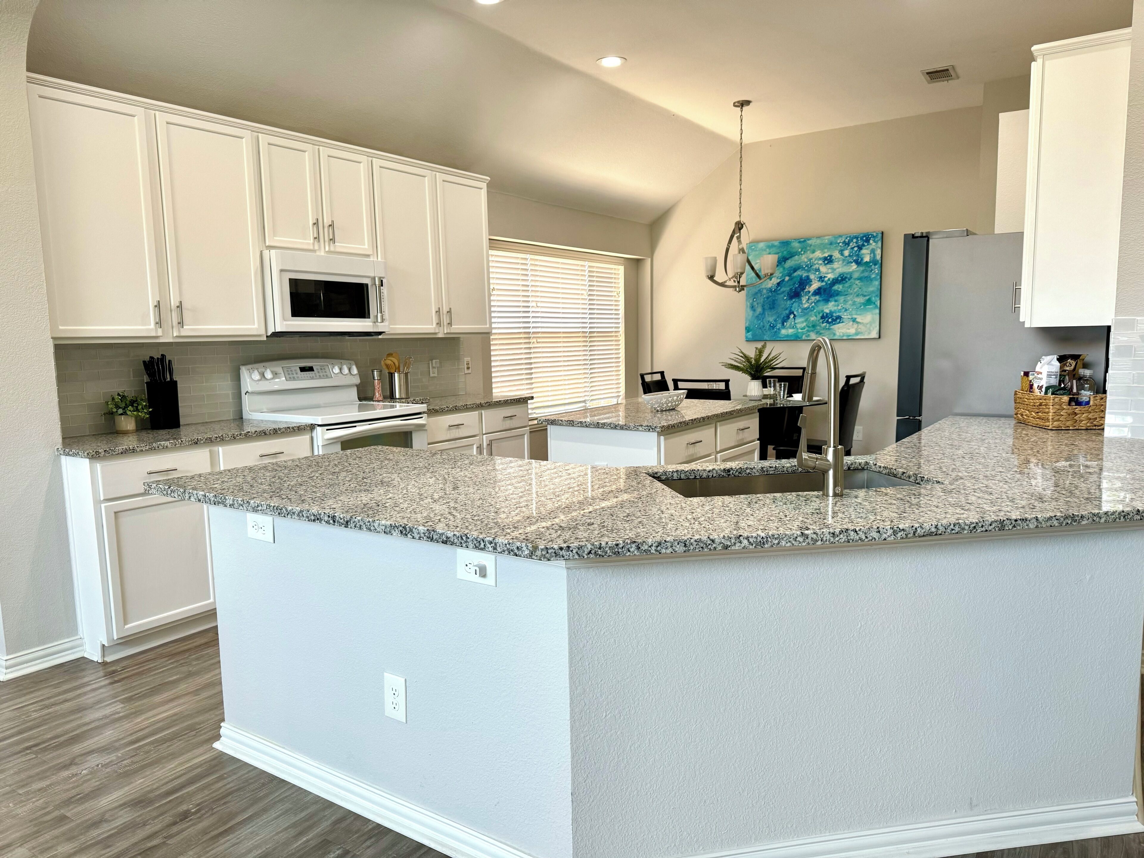 A modern kitchen with white cabinetry, granite countertops, a built-in oven, and a large island with a sink.