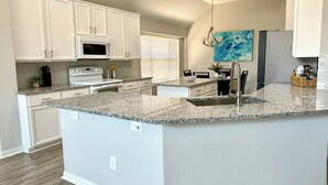 A modern kitchen with white cabinetry, granite countertops, a built-in oven, and a large island with a sink.