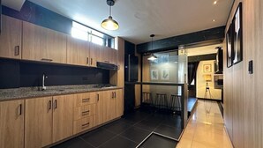 A modern kitchen with wooden cabinets, a black countertop, and a tiled floor. There is a bar area with stools and a glass partition. - Luxury apt with jacuzzi near downtown  (Santa Rosa de Cabal)