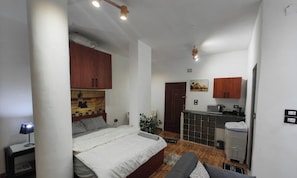 Une piĂšce de taille modeste comprenant un lit, une petite kitchenette et une porte donnant sur une autre piĂšce.