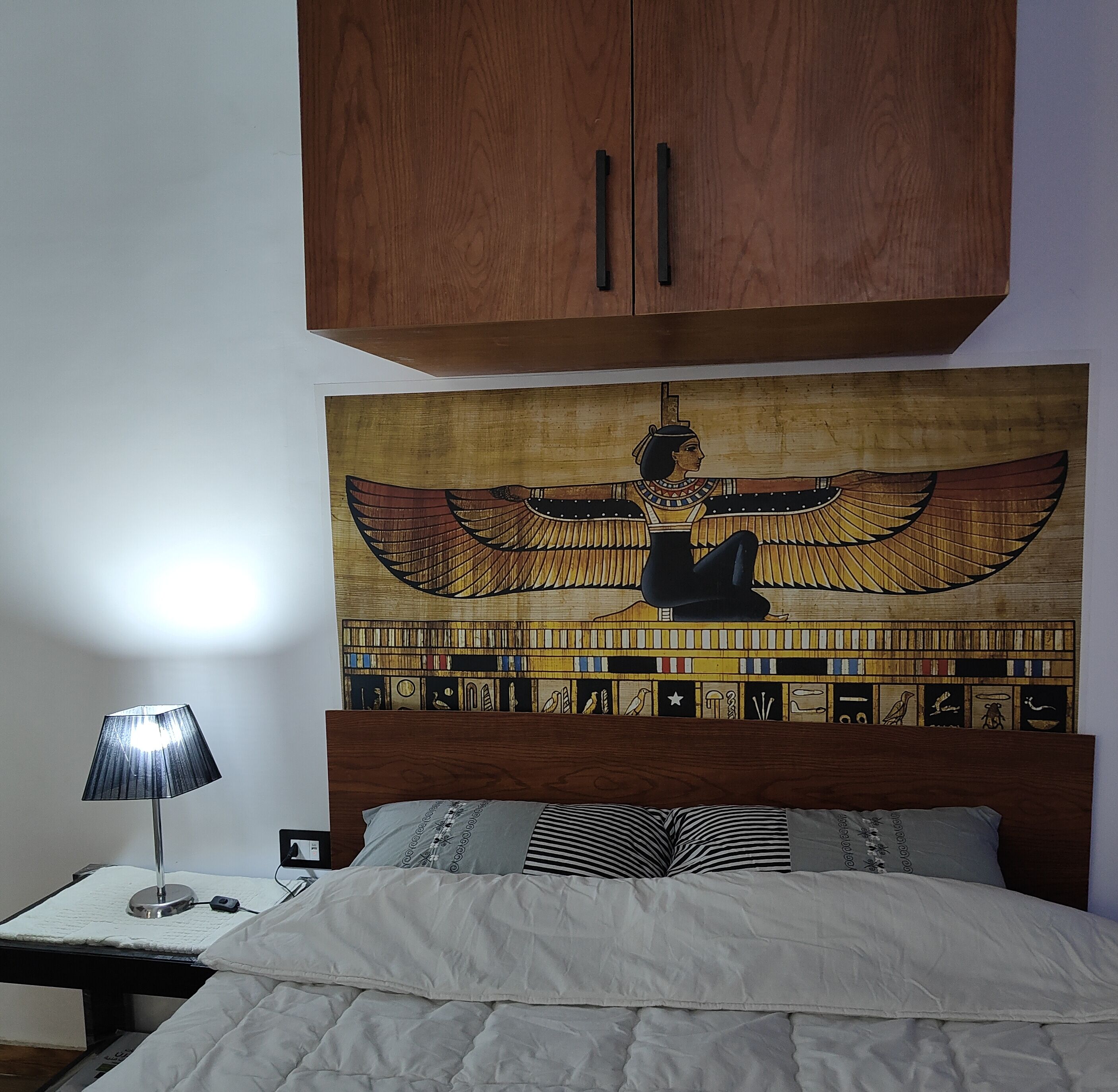 A bedroom with a bed, a nightstand, a lamp, and a wall tapestry.