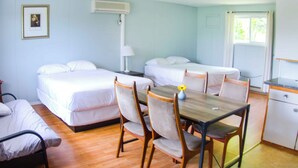 Una habitación con dos camas individuales, una mesa de comedor de madera con sillas, una pequeña cocina y un ventanal con cortinas.