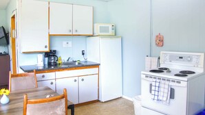 Una cocina compacta con armarios blancos, un microondas, una estufa y un lavamanos.