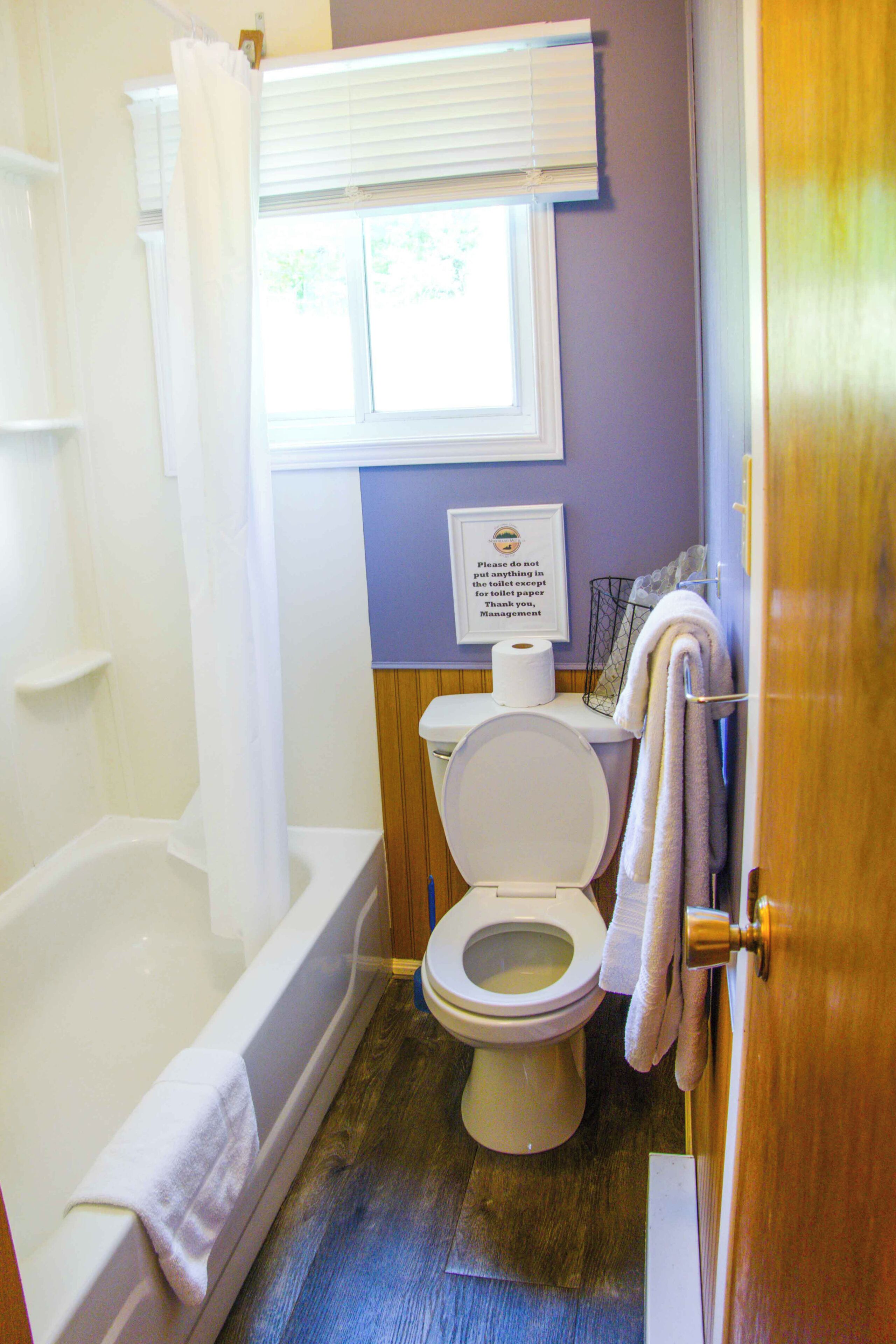 Een badkamer met een bad, toilet en een raam met zonwering.