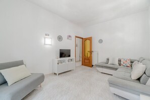A modern living room with a grey sofa, a white cabinet with a TV, and a wooden door. - GuestHost - 85 sqm apartment for 6 people, located on the first floor of a building with an elevator (not suitable for people with disabilities). It features two balconies and is situated in a very quiet neighborhood, just steps from Parco Dora, full of  (Torino)