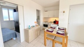 Une chambre de taille modeste comprenant un lit, une petite kitchenette et un coin repas avec une table dressée pour deux personnes.