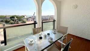 Un balcon avec une table dressée pour deux personnes, donnant sur un quartier résidentiel avec des maisons et de la verdure.