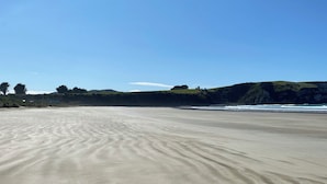 A sandy beach with gentle waves, a clear sky, and distant green hills.
