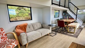 A modern living room with a sofa, a dining table, and a staircase.