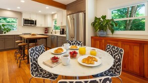 Une cuisine moderne avec des meubles blancs, des appareils en acier inoxydable et un coin repas agrémenté de chaises à motifs.