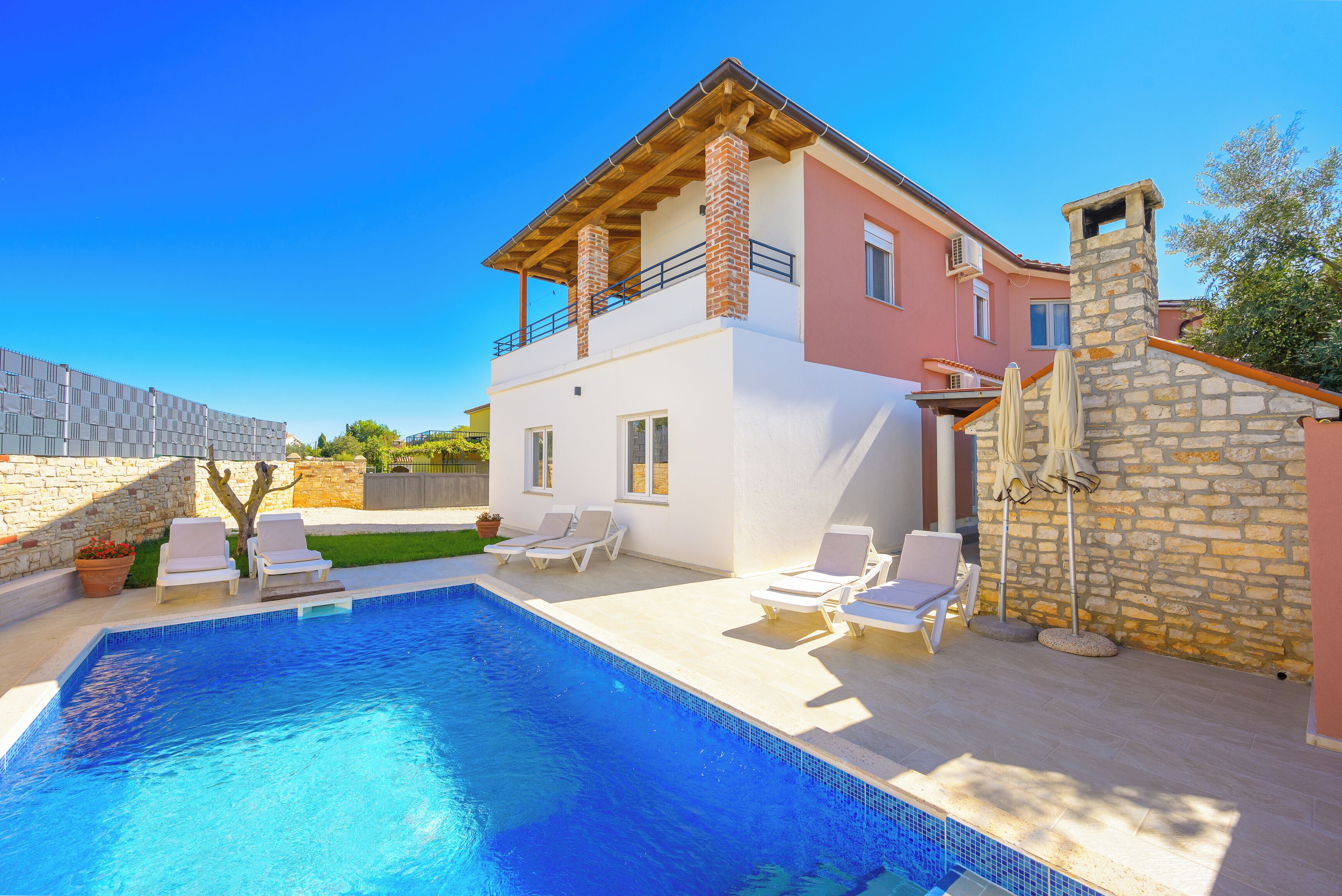 A two-story house with a swimming pool, outdoor seating, and a stone wall.