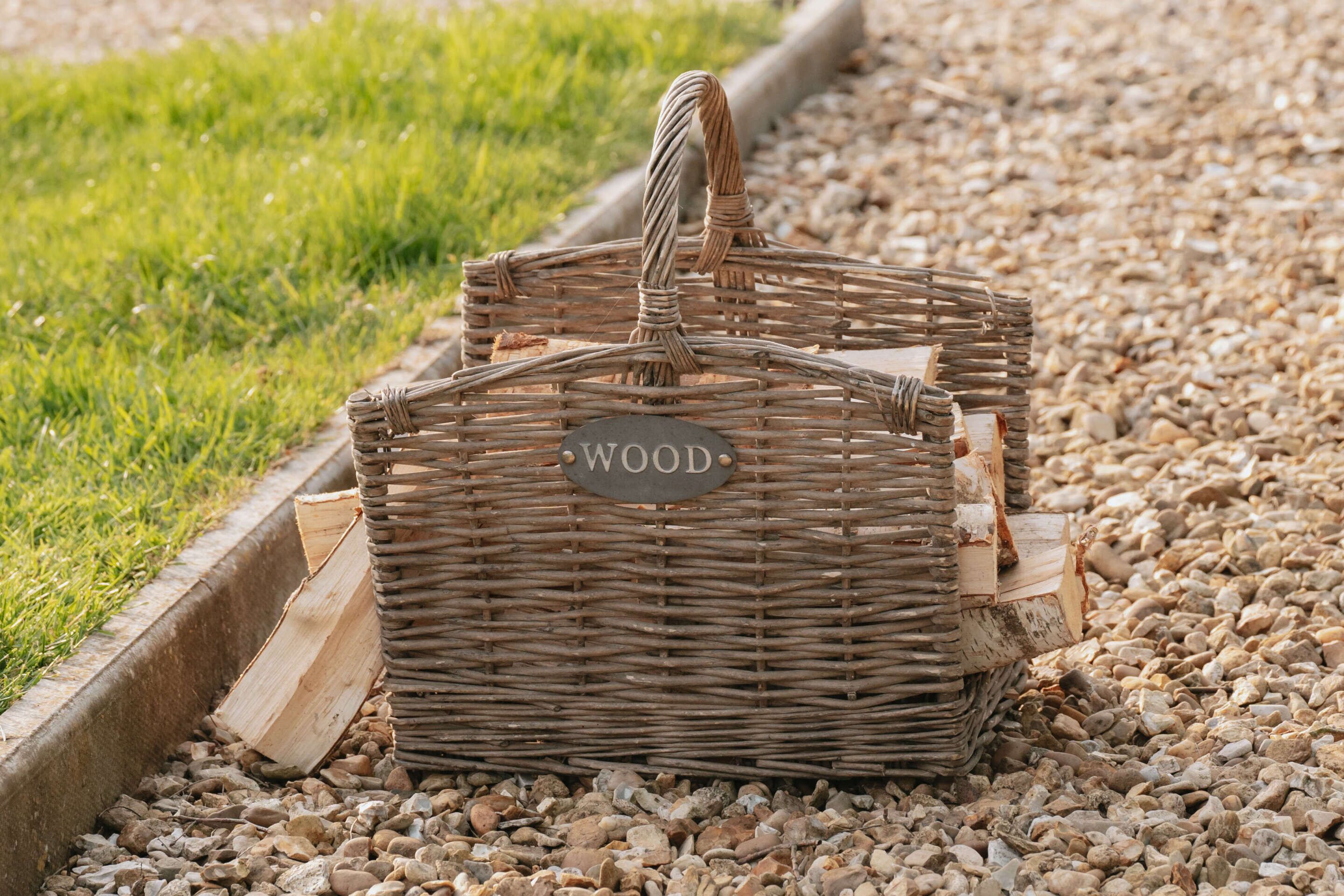 Una cesta de mimbre con la etiqueta 'WOOD' sobre un camino de grava con césped a un lado.