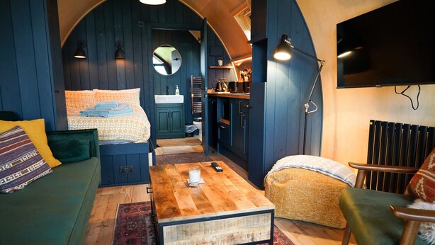 A cozy room with a wooden coffee table, a sofa, a chair, and a kitchen area with a TV and a radiator.