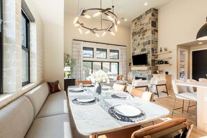 A modern dining area with a marble table, comfortable seating, a stone accent wall, and a large window. - Deer Valley East Village, Free Ski Shuttle, Near the Lake, Private Hot Tub (Heber City)
