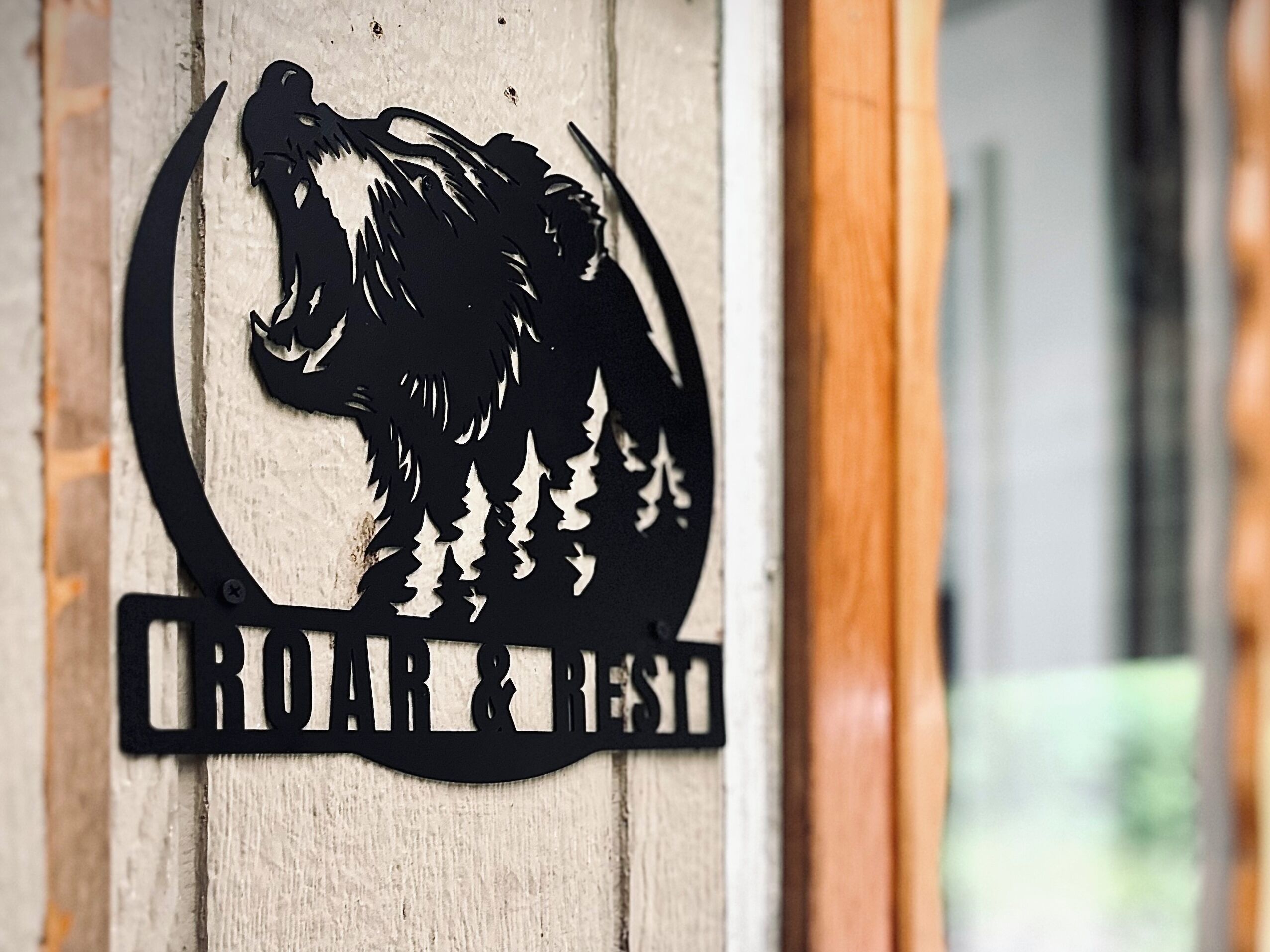Puinen kyltti, jossa on musta, karjuvan eläimen siluetti ja teksti: ”CROAR & REST”.