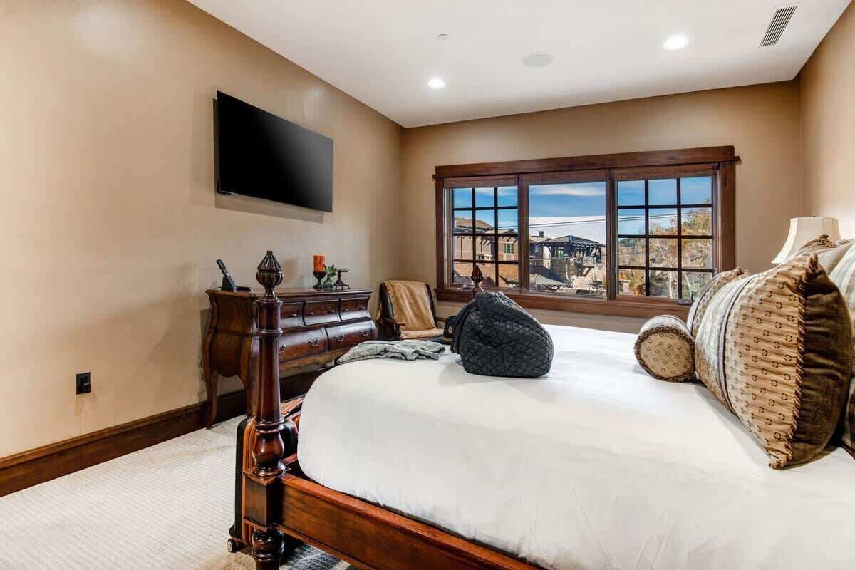 Een slaapkamer met een groot bed, een kaptafel, een aan de muur bevestigde televisie en een raam met uitzicht.