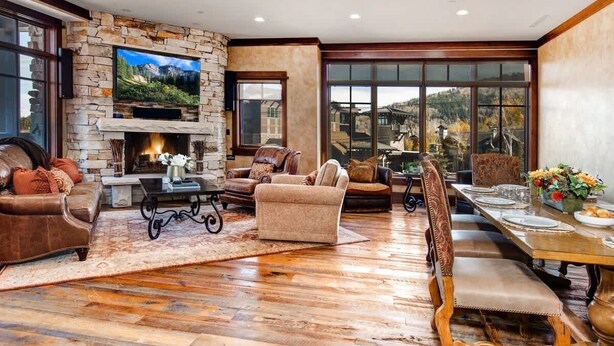 A spacious living room with a stone fireplace, leather furniture, and a dining area with a large window. - Abode at Silver Summit, ski-in/ski-out, hot tub, pool table, Silver Lake (Park City)