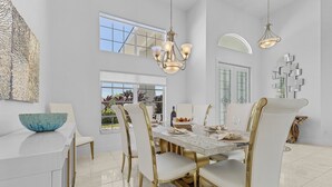 Een moderne eetruimte met een grote tafel, witte stoelen en gouden accenten.