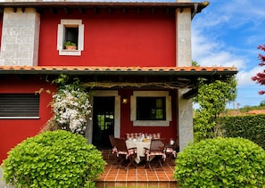 A red building with a tiled patio, a table with chairs, and a small window.