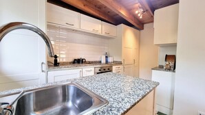 A modern kitchen with white cabinets, granite countertops, stainless steel sink, and a wooden ceiling. - La Curuxa House in Vidiago, Llanes (Vidiago)